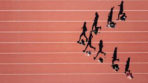 Top-down view of runners training along a bright terracotta running track in warm morning sunlight