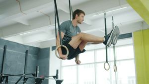 Athlete holding a straight-arm L-sit on wooden gymnastic rings in a sunlit gym