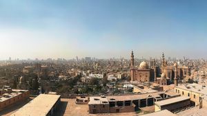 Panoramic view of historic sandstone mosques and the Cairo skyline under a bright blue sky