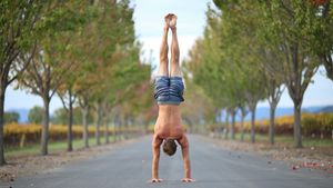 Athletic man holding a straight freestanding handstand in the center of a sunlit tree-lined road