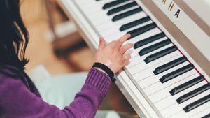 A child in a purple sweater plays a white Yamaha piano with one hand