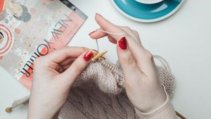 A person hand-knitting a beige woolen garment with wooden circular knitting needles