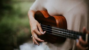 Close-up of a person's hands strumming a brown wooden four-string ukulele outdoors