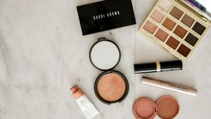 Assorted cosmetic powders, brushes, and lipsticks arranged on a clean vanity counter