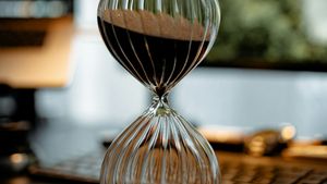 Close-up of a ribbed glass hourglass sitting on a sunlit desk