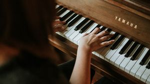 A woman plays a wooden Yamaha upright piano with both hands