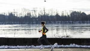 A woman running along a snow-lined river trail on a crisp winter morning