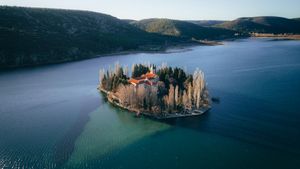 Aerial view of Visovac Monastery on an island in a calm lake surrounded by trees and mountains