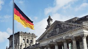The German flag flies above the Reichstag building in Berlin under a blue sky