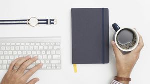 An open notebook with a pen beside a cup of coffee on a wooden desk