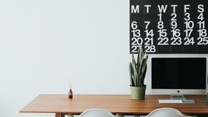 A clean minimalist wooden desk with a notebook, pen, watch, and coffee cup
