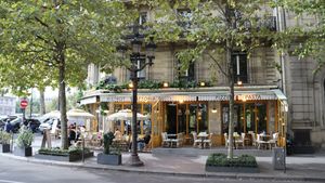 Chairs and round tables outside a Parisian street café under an awning