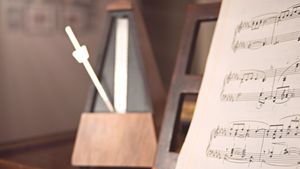 A wooden mechanical metronome sits next to open sheet music marked with pencil fingerings