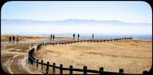 Hikers walking along a fenced trail at Stanford Dish with golden hills and a hazy skyline