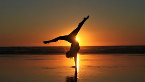 Silhouette of a person doing a one-handed handstand on a beach at sunset