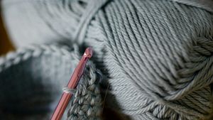 A skein of yarn and an ergonomic crochet hook resting on a clean wooden workspace