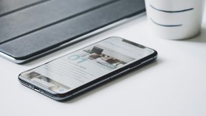 iPhone resting beside a closed tablet cover and ceramic mug on a white desk