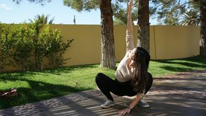 Woman holding a deep squat with one arm reaching overhead in a sunlit yard